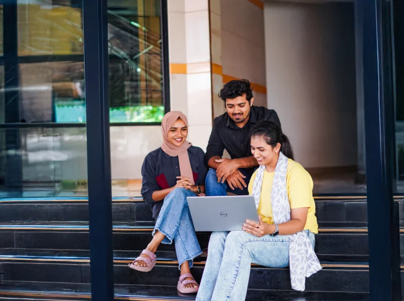Students sitting on campus stairs working together on a laptop during a digital marketing course in Kochi.
